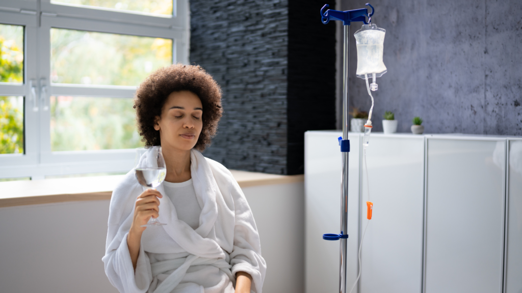 A patient receiving IV therapy while drinking a fresh glass of water